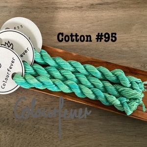 Puede incluir: Tres madejas de hilo de bordar de algod&oacute;n verde azulado y verde en una bandeja de madera. El hilo est&aacute; etiquetado como "Colourfever #95".