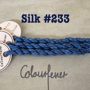 Könnte beinhalten: Drei Spulen blauer Seiden-Stickgarn mit schwarzem Schimmer, beschriftet mit "Colourfever" und "#233".