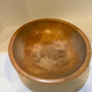 May include: A round wooden bowl with a warm, natural wood tone. The bowl has a smooth, polished interior and a slightly raised rim. The wood grain is visible, adding to the rustic charm. This bowl is suitable for serving or display.