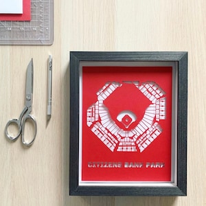 May include: A black framed shadow box with a red paper cutout of Citizens Bank Park, a baseball stadium in Philadelphia, Pennsylvania. The stadium is outlined in white and the text "CITIZENS BANK PARK" is printed in white at the bottom.