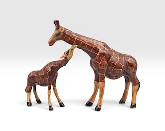 May include: A glossy ceramic figurine set featuring a large adult giraffe and a smaller calf giraffe. Both animals have a rich brown coat with a distinct white grid pattern, tan lower legs, and black hooves, standing in a side-facing position.