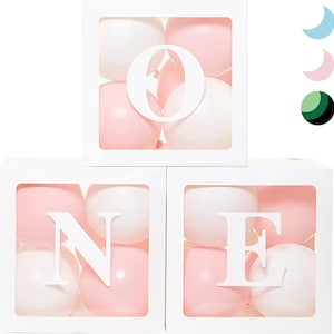 May include: Three white boxes with clear plastic windows filled with pink and white balloons. Each box has a white letter cut out, spelling out the word "ONE".