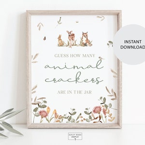 Pode incluir: Uma placa emoldurada com uma moldura de madeira clara. A placa tem o texto "Adivinhe quantos biscoitos de animais estão no pote" em uma fonte caprichosa. Ilustrações em aquarela de animais da floresta e folhagens decoram a placa.