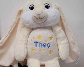 May include: A cream-colored plush bunny with large blue eyes and a blue embroidered name "Theo" on its chest. The bunny is surrounded by yellow embroidered stars.