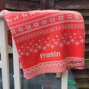 May include: Red and white knitted baby blanket with a snowflake and reindeer pattern. The blanket has the name "Franklin" embroidered on it. The blanket is made by Lilyjoes Creations.