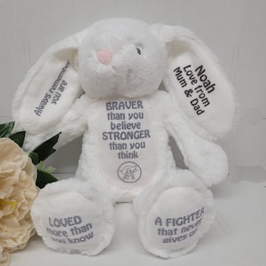 Puede incluir: Un conejito de peluche blanco con texto bordado. El conejito tiene orejas largas con las frases "Always remember you are" y "Noah Love from Mum & Dad". El cuerpo tiene "BRAVER than you believe STRONGER than you think" y "LOVED more than you know" y "A FIGHTER that never gives up".