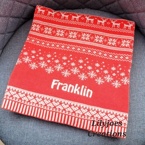 Pode incluir: Cobertor de malha vermelho e branco com um padrão festivo de renas, flocos de neve e desenhos geométricos. O nome "Franklin" é exibido em branco, com "Lilyjoes Creations" na parte inferior. Um item de decoração para casa aconchegante e sazonal.