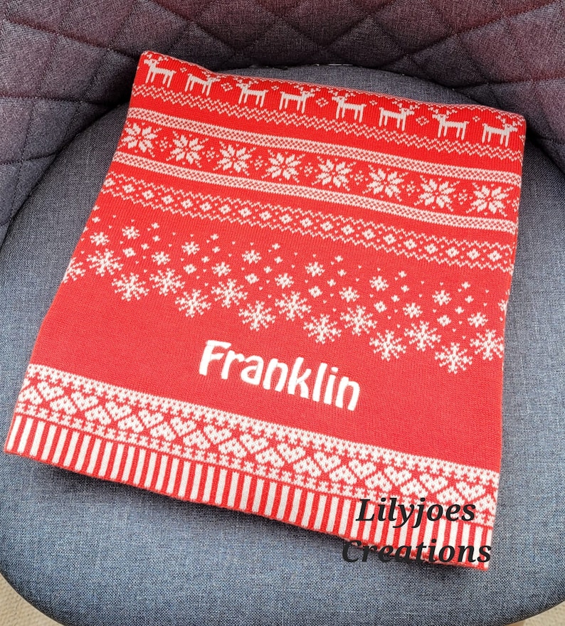 May include: Red and white knitted throw blanket with a snowflake and reindeer pattern. The blanket is personalized with the name "Franklin".