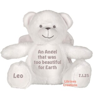 Pode incluir: Urso de peluche branco com asas de anjo, a inscrição "An Angel that was too beautiful for Earth" e o nome "Leo" na pata. A data "7.1.25" e o texto "Lily Joes Creations" também são visíveis.