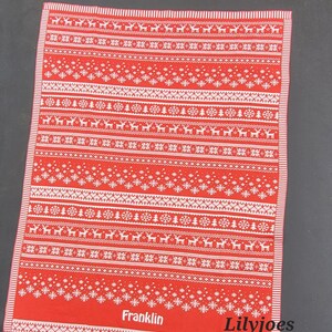 May include: Red and white Christmas themed kitchen towel with a Scandinavian pattern of snowflakes, reindeer, and trees. The towel has the name "Franklin" and the text "Lilyjoes Creations" printed on it.