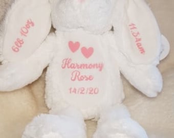 May include: A white plush bunny with pink accents on the nose and inner ears. The bunny has embroidered text on the ears and chest, including the name "Harmony Rose" and the date 14/2/20. A small card with the text "LilyJoe's Creations" is at the bottom.