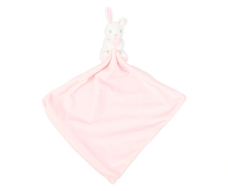 Peut inclure: Une couverture rose pour b&eacute;b&eacute; avec un lapin blanc attach&eacute;. Le lapin a des oreilles roses et un nez rose.