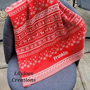 May include: Red and white knitted throw blanket with a snowflake and reindeer pattern. The blanket has the name "Franklin" embroidered on it.