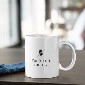 May include: White ceramic mug with a black microphone icon with a line through it and the text "You're on mute..." printed on the front.