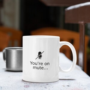 May include: White ceramic mug with a black microphone icon with a line through it and the text "You're on mute..." printed on the front.