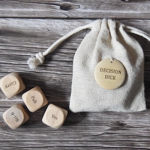 May include: A set of wooden dice with different words on each side, including "Curry", "Pub", "Yes", and "Selfie". The dice are in a small white drawstring bag with a round tag that says "Decision Dice".