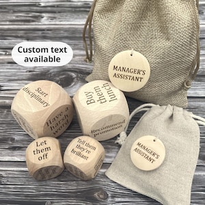May include: A selection of wooden dice with engraved phrases, accompanied by small hessian bags and wooden tags. The dice display phrases such as "Buy them lunch" and "Start disciplinary." The tags and bags read "MANAGER'S ASSISTANT."