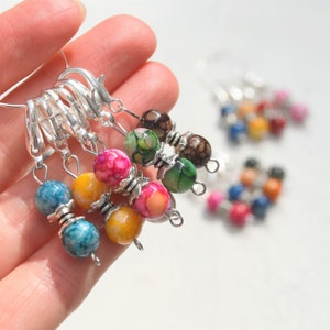 May include: A set of colourful agate stitch markers with silver rings. The markers are strung on a silver chain and feature a variety of colours and patterns.