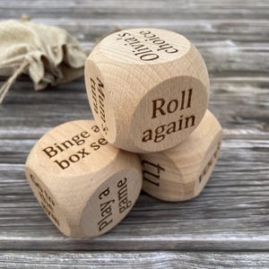 May include: Three wooden dice with different phrases engraved on each side. The phrases are "Olivia's choice", "Mum's turn", "Binge a box set", "Roll again", "Go to bed", and "Play a game".