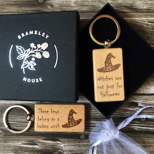 May include: Two wooden keyrings with a witch hat design and engraved text. The keyring on the left says "These keys belong to a badass witch". The keyring on the right says "Witches are not just for Halloween".