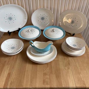 May include: A vintage set of white and blue patterned dinnerware with a starburst design. The set includes plates, bowls, a gravy boat, and serving dishes.
