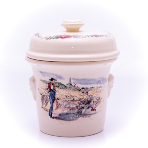 May include: A white ceramic jar with a lid, featuring a hand-painted scene of a man in a field with a church in the background. The jar has a floral design around the top and the signature "H. Lava" on the bottom.