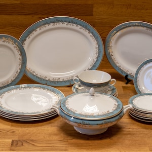 May include: A set of blue and gold rimmed porcelain dinnerware, including a large oval platter, a round serving bowl with a lid, a soup bowl, and several plates of varying sizes.