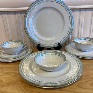 May include: Set of four white porcelain soup bowls with green and blue floral trim. The bowls are arranged on three matching plates with the same trim.