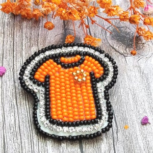 May include: Orange and black beaded t-shirt design with rhinestones around the edges.