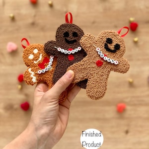 May include: Three gingerbread man ornaments in shades of brown, tan, and white, each with a red heart and a beaded name necklace. The ornaments have a loop for hanging and are decorated with a smiling face. The text "Finished Product" and "Punchatelier" are visible.