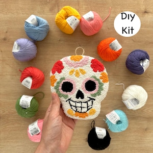 May include: DIY kit for a colorful, embroidered sugar skull. The kit includes a variety of yarn colors, including white, black, orange, pink, green, blue, and yellow. The yarn is wrapped around small cardboard spools. The kit also includes a pre-punched canvas with a sugar skull design.
