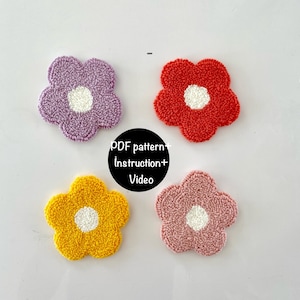 May include: Four colorful, flower-shaped, tufted coasters. The coasters are in shades of purple, red, yellow, and pink, each with a white center. The image includes the text "PDF pattern + Instruction + Video".