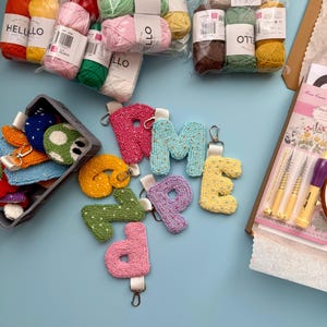May include: A selection of craft items, featuring bundles of colourful yarn, letter keyrings, and a basket of small, embroidered pieces. The yarn is packaged in various colours, and the keyrings are in shades of pink, blue, yellow, and green.