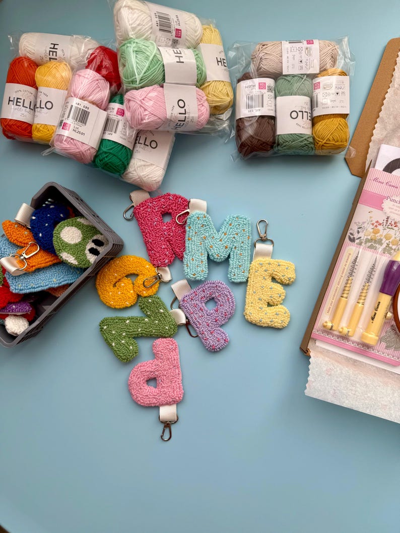 May include: A selection of craft items, featuring bundles of colourful yarn, letter keyrings, and a basket of small, embroidered pieces. The yarn is packaged in various colours, and the keyrings are in shades of pink, blue, yellow, and green.