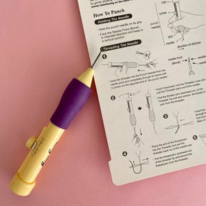May include: A close-up of a purple and yellow punch needle tool with instructions on how to thread the needle. The instructions include illustrations of the steps involved in threading the needle.