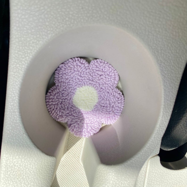 May include: A purple and white flower-shaped cup coaster. The coaster is made of yarn and has a white center.