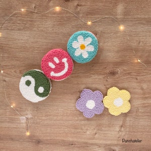 May include: Five colorful round wool punch needle wall hangings with different designs. The designs include a yin yang symbol, a smiley face, a daisy, a purple flower, and a yellow flower.