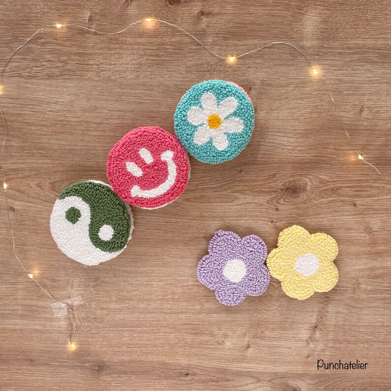 May include: Five colorful round wool punch needle wall hangings with different designs. The designs include a yin yang symbol, a smiley face, a daisy, a purple flower, and a yellow flower.