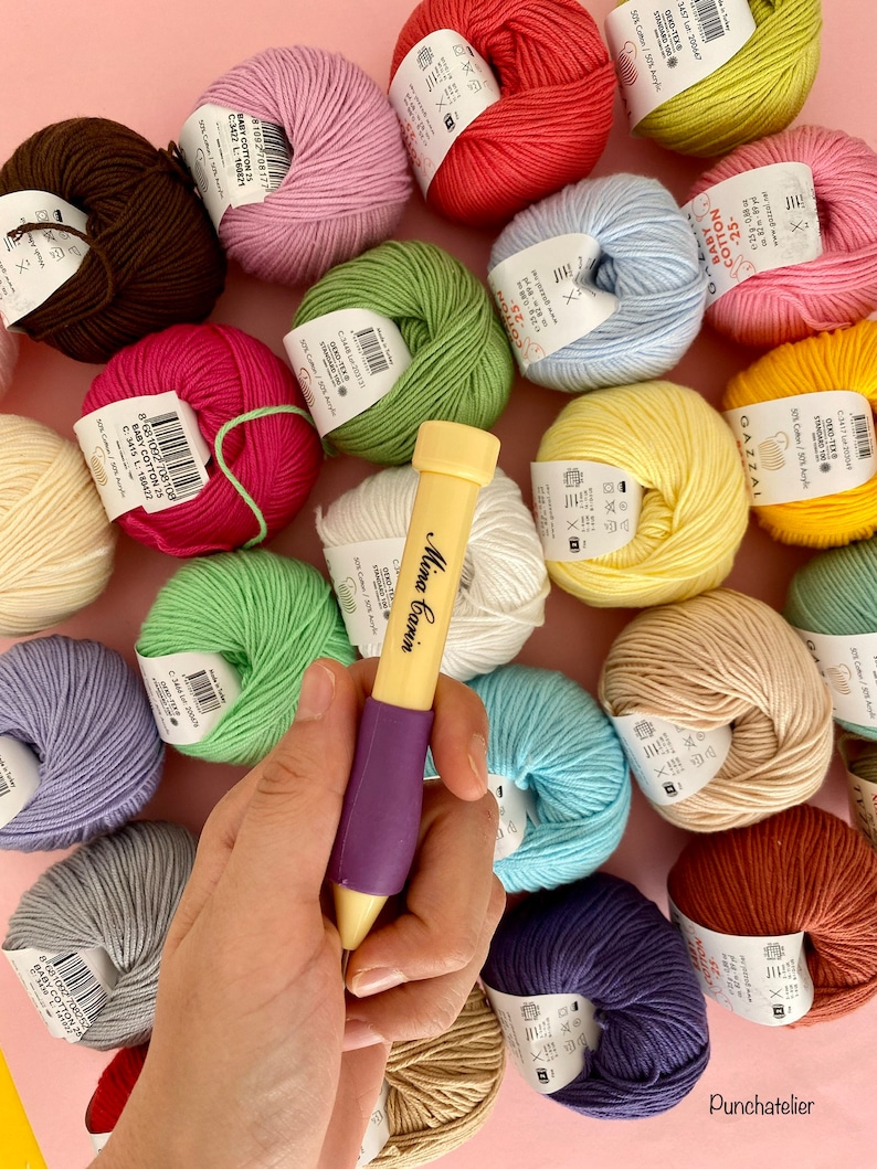May include: A close-up of a purple and yellow crochet hook with a variety of colorful yarn balls in the background. The yarn balls are arranged in a circle around the crochet hook. The yarn balls are all different colors, including pink, red, green, blue, yellow, and brown.