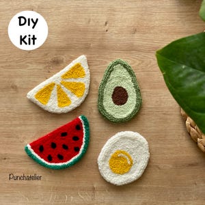 May include: A DIY kit featuring four colorful, textured fruit and food-themed coasters. The set includes a lemon slice, avocado, watermelon slice, and a fried egg. The text "DIY Kit" and "Punchatelier" are visible.