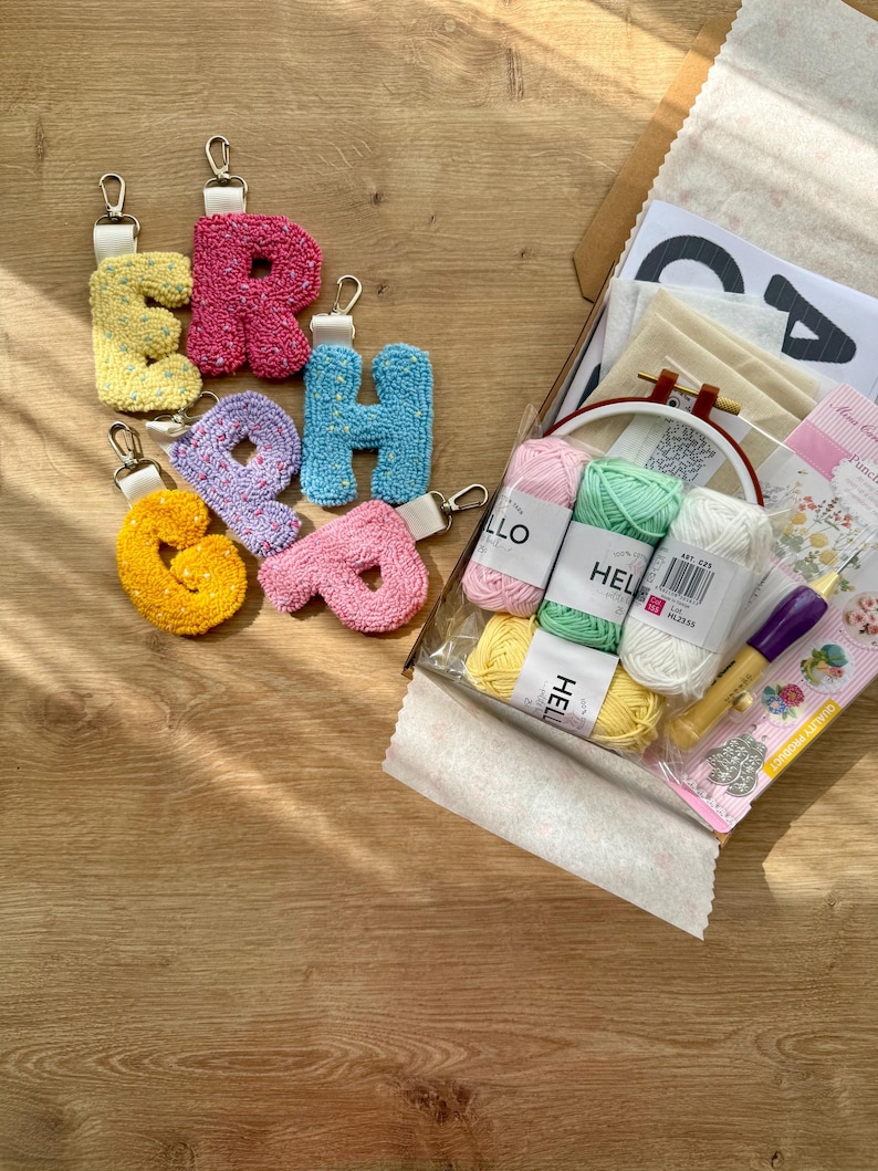 May include: A selection of colourful, textured letter keychains spelling "ERAH" in yellow, pink, blue, purple, and orange. The keychains are shown with a craft kit containing yarn, a hoop, and other supplies.