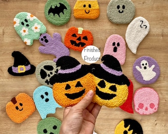 May include: A collection of 16 Halloween-themed punch needle crafts. The crafts are in the shape of pumpkins, ghosts, bats, candy corn, and witches' hats. The crafts are made with colourful yarn and are displayed on a wooden surface.