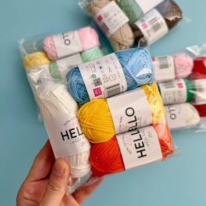 May include: A selection of colourful yarn bundles in clear packaging. The yarn includes shades of yellow, orange, red, pink, blue, green, and white. Each ball of yarn has a label that reads "HELLO petite ball".