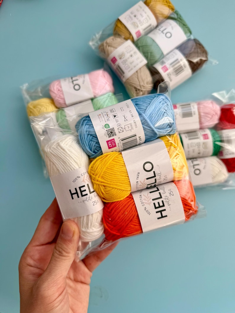 May include: A selection of colourful yarn bundles in clear packaging. The yarn includes shades of yellow, orange, red, pink, blue, green, and white. Each ball of yarn has a label that reads "HELLO petite ball".