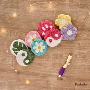 May include: A set of seven colorful punch needle embroidery hoops with various designs, including flowers, leaves, and a yin yang symbol. A purple punch needle tool is also included.