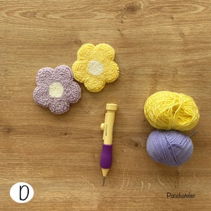 May include: Two punch needle flower designs, one purple and one yellow, with white centers. A punch needle tool and two balls of yarn, one purple and one yellow, are also shown. The text "Punchatelier" is visible in the bottom right corner.