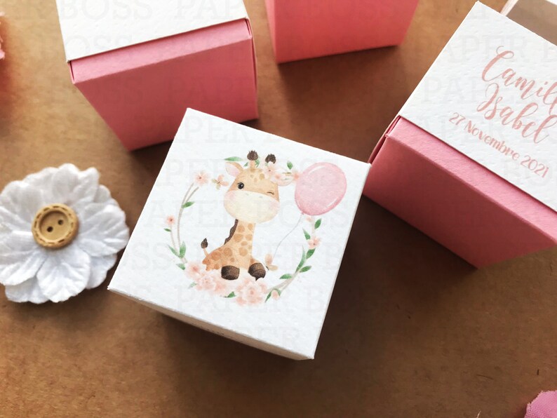 Peut inclure: Une bo&icirc;te &agrave; drag&eacute;es blanche avec un couvercle rose. La bo&icirc;te est illustr&eacute;e d'une aquarelle repr&eacute;sentant une girafe avec un ballon rose. Le texte sur la bo&icirc;te est "Camila Isabel 27 Noviembre 2021".