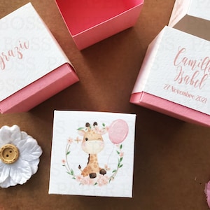 Peut inclure: Trois bo&icirc;tes &agrave; drag&eacute;es roses et blanches avec un motif de girafe, de fleurs et de ballon. Une bo&icirc;te dit "Grazie" et une autre dit "Camilla Isabel 27 Novembre 2021".