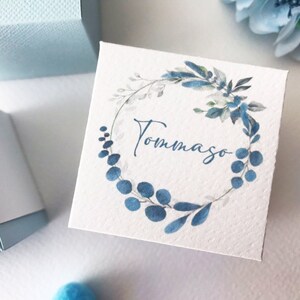 May include: A white gift box with a blue watercolor wreath and the name "Tommaso" written in blue cursive.