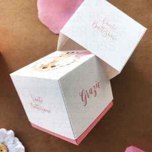 Peut inclure: Bo&icirc;te &agrave; drag&eacute;es blanche avec un ruban rose et le texte "Santo Battesimo" et "Grazie" en cursive. La bo&icirc;te est d&eacute;cor&eacute;e d'un motif floral avec une illustration aquarelle d'un cerf.